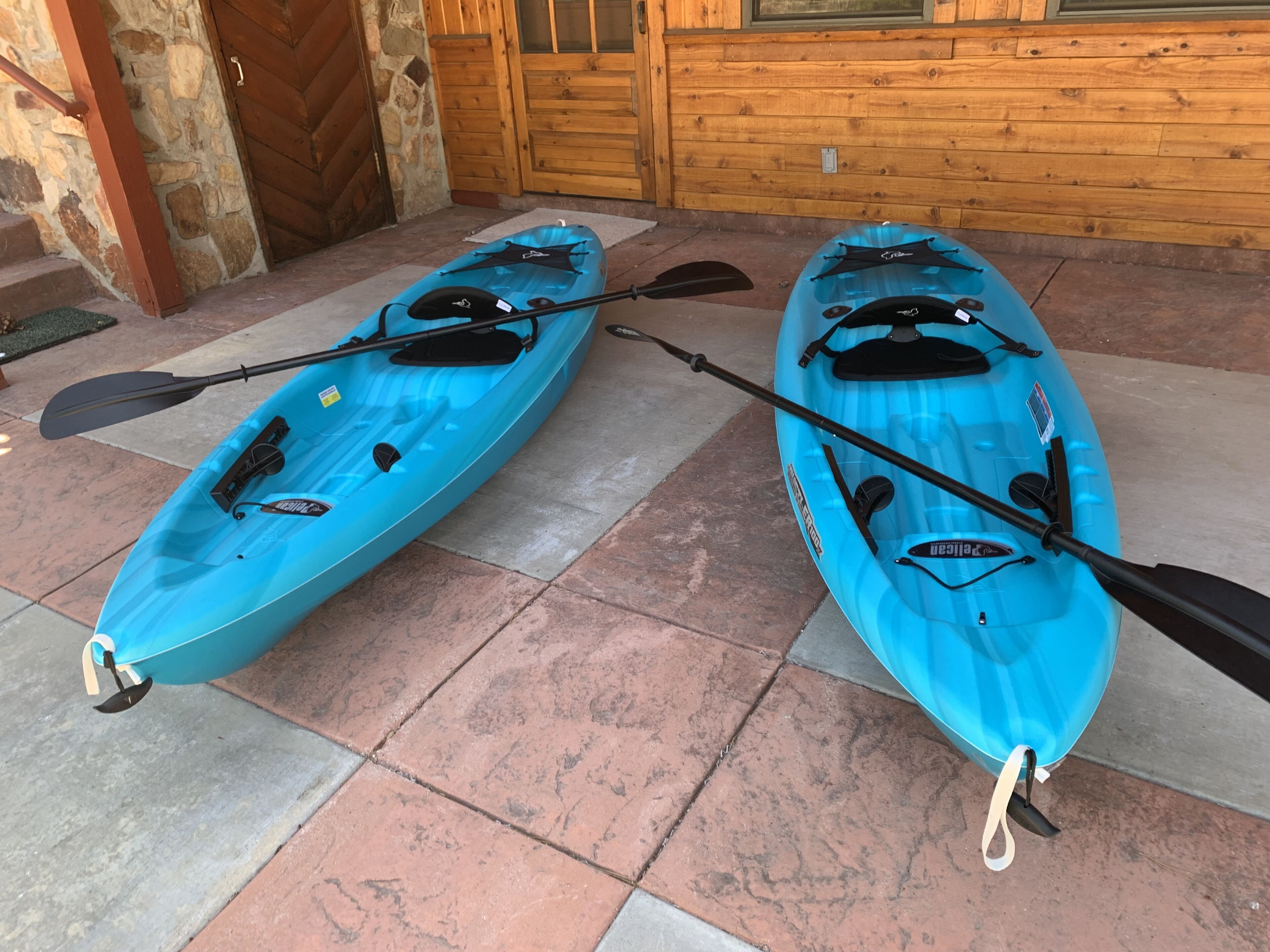 Two kayaks with paddles and life vests on a tiled patio.