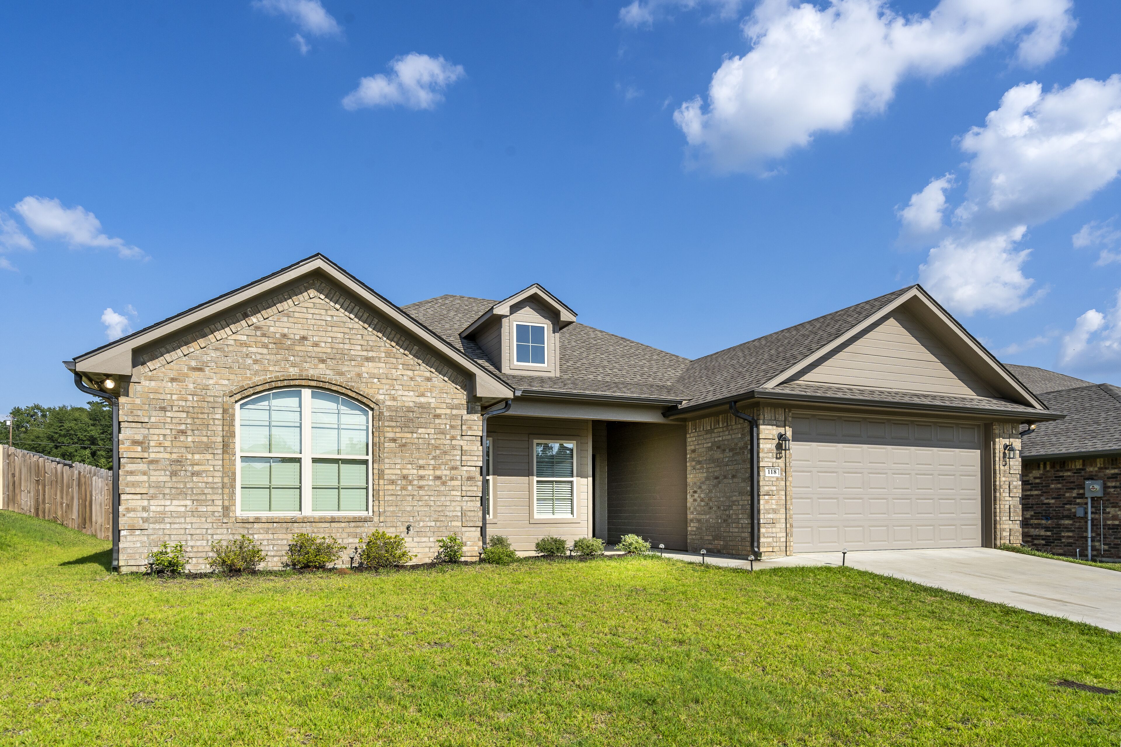 A two-story house with a garage, a large arched window, and a well-maintained lawn.