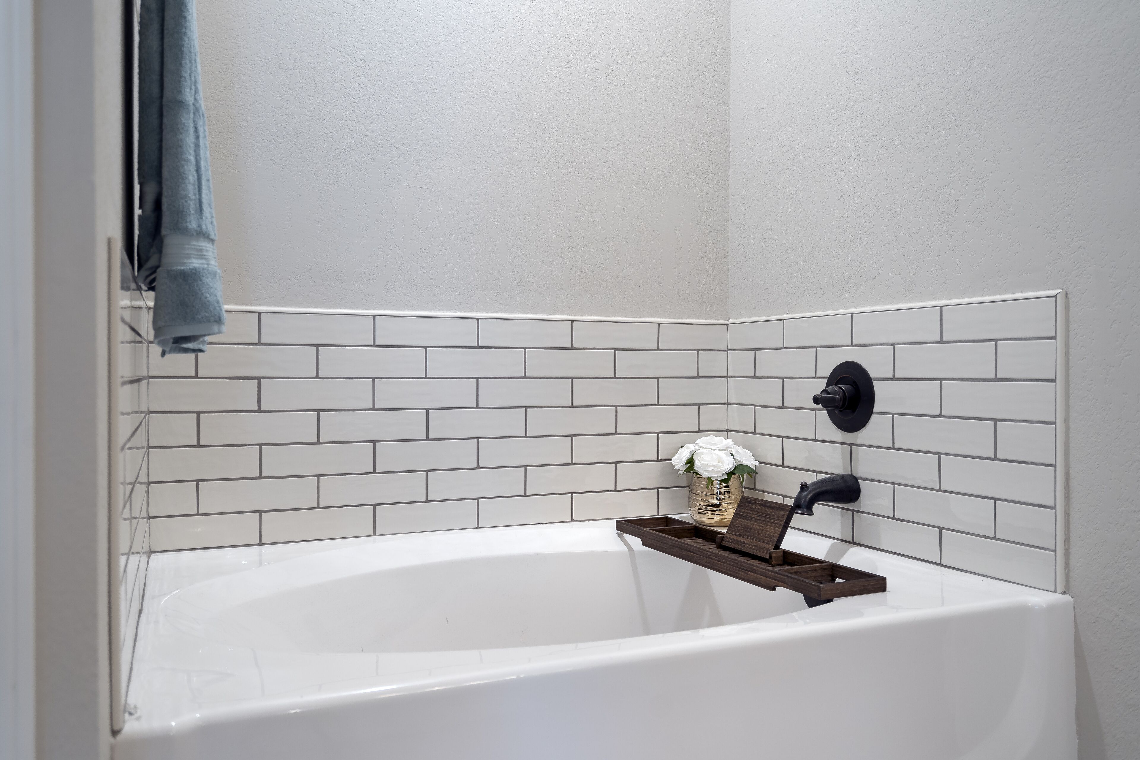 Eine weiße Badewanne mit einem Holztablett und einem Blumenstrauß.