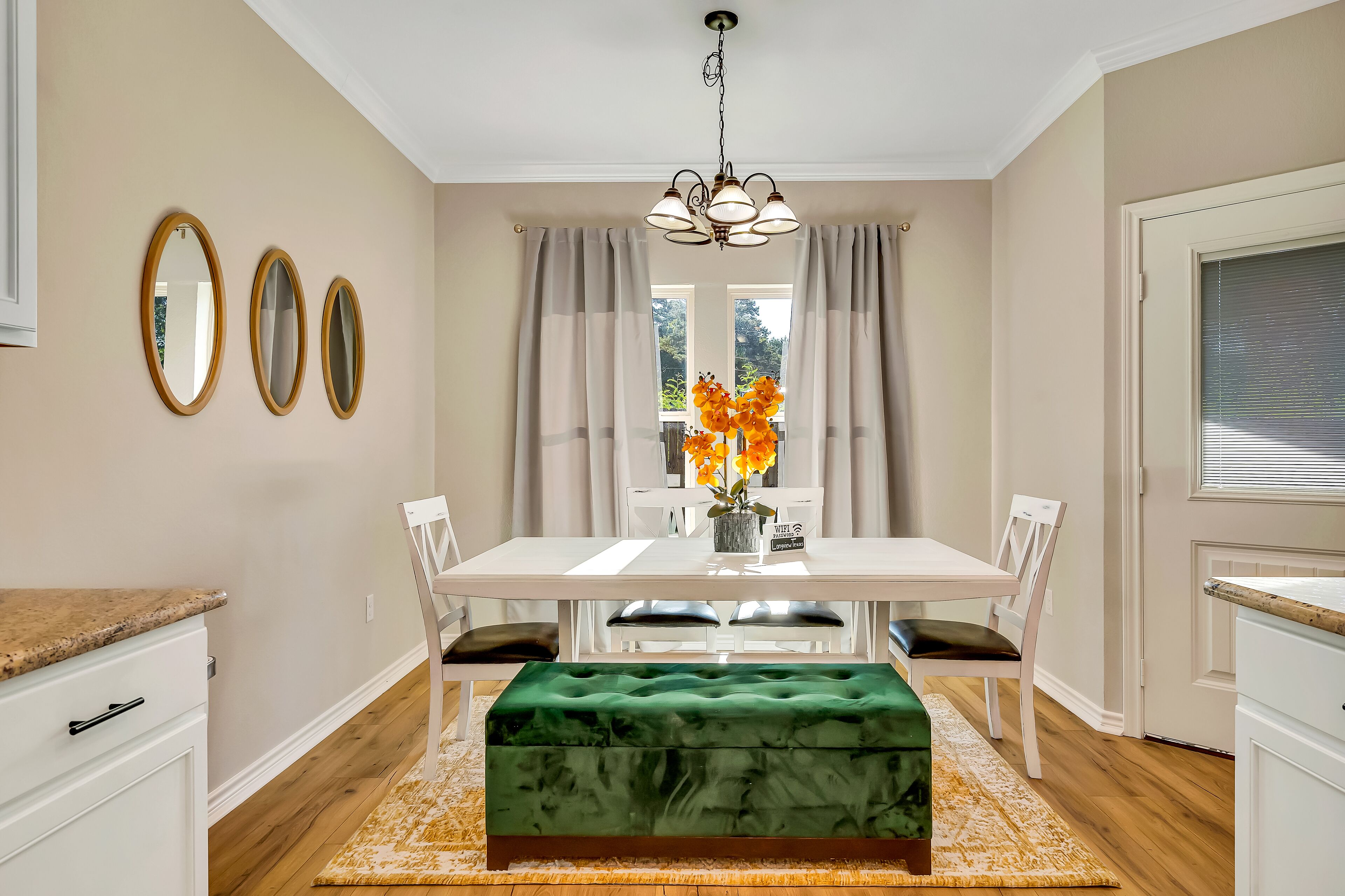 A dining area with a white table, green upholstered bench, and three wall-mounted mirrors.