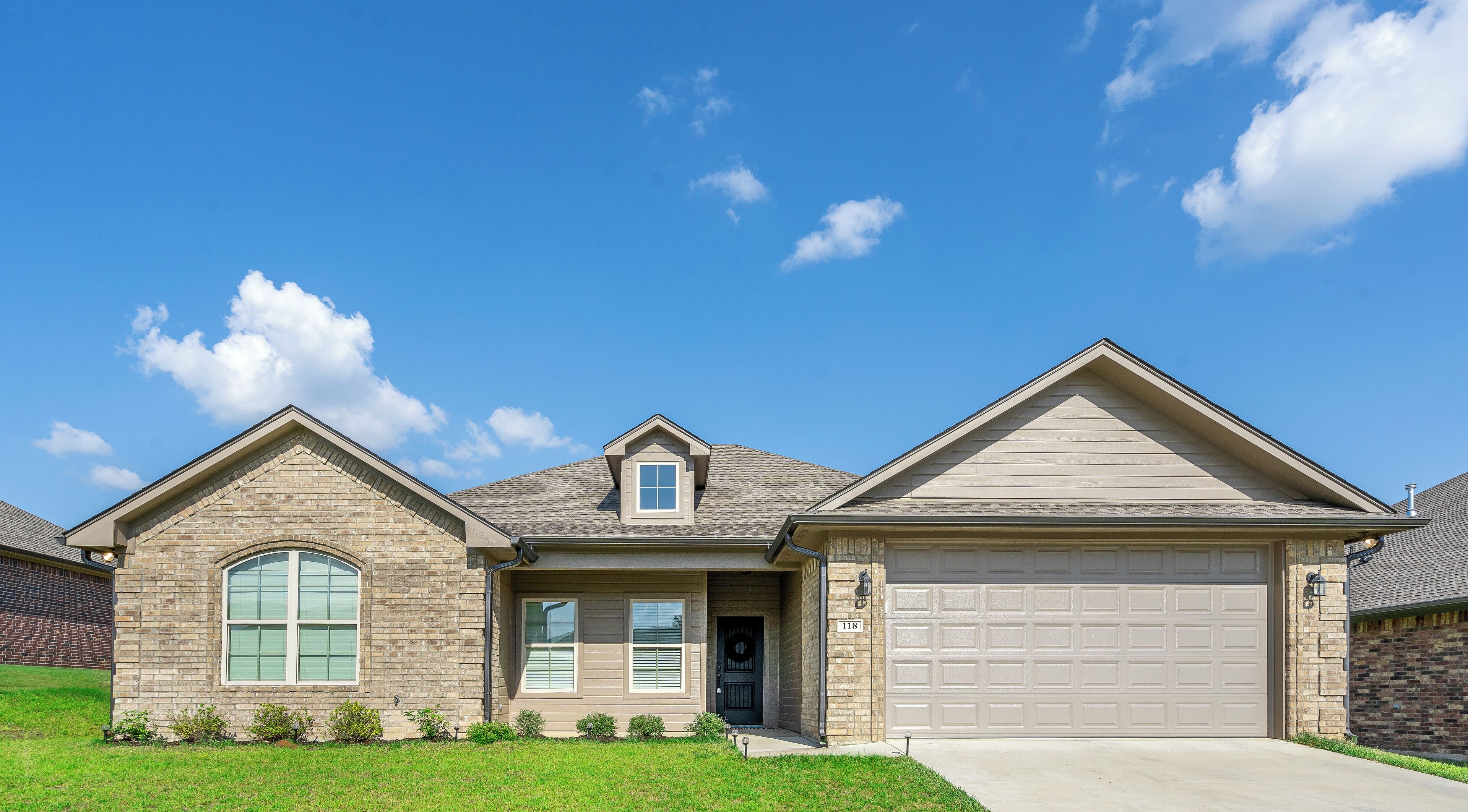 Una casa de dos pisos con garaje, un pequeño porche y un césped bien cuidado.