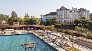 A swimming pool with sun loungers and umbrellas, surrounded by trees and a large historic building in the background. - Curia Palace Hotel Spa and Golf (Anadia)