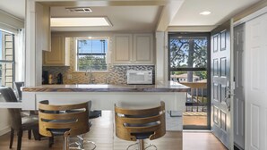 Una cocina moderna con una isla central, taburetes de bar y vistas a través de la puerta abierta.