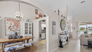 Uma sala de estar ampla com uma mesa de jantar de madeira, um banco e uma cozinha ao fundo.
