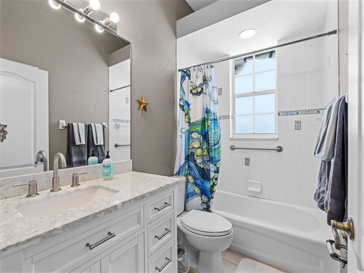 A bathroom with a white sink, vanity, and a bathtub. There is a window above the bathtub and a starfish decoration on the wall.