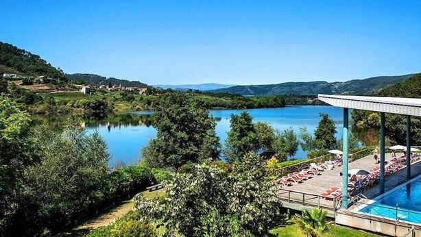 Zona de piscina con sillones de descanso y una zona de estar cubierta con vistas a un lago.