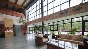 Un vestíbulo amplio con techo alto, ventanas grandes y una recepción.