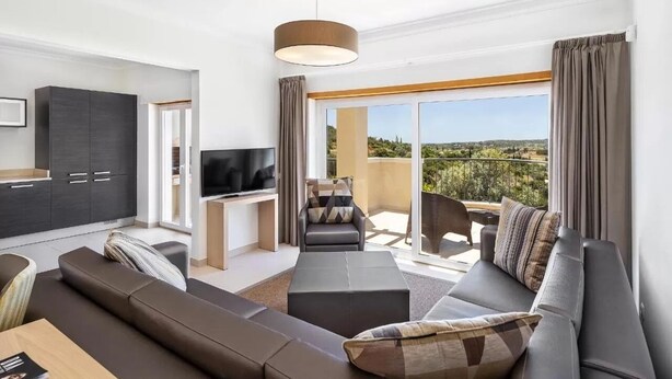 A modern living room with a sofa, a TV, and a balcony with a view. - Vale Da Ribeira Residences (Portimao)