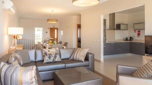 A modern living room with a grey sofa, glass coffee table, and a kitchen area with grey cabinets and a microwave. - Vale Da Ribeira Residences (Portimao)