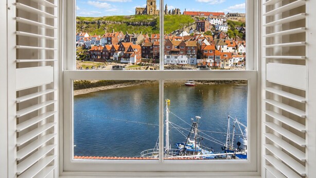 A window with shutters, a view of a town with buildings and a church, and a river with boats. - Whitby Sea View Cottage Harbour Views Quiet Cragg (Whitby)