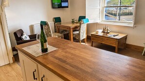 A cozy room with a wooden dining table, a TV mounted on the wall, and a window with a scenic view. - Whitby Sea View Cottage Harbour Views Quiet Cragg (Whitby)