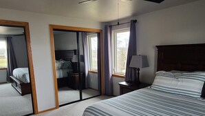 A bedroom with a large bed, a bedside table with a lamp, a mirror, and a window with curtains.