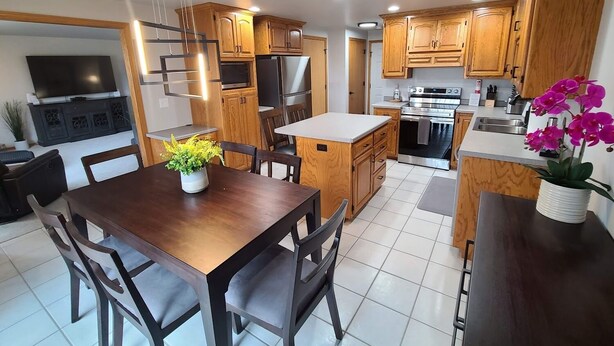 A modern kitchen with wooden cabinets, stainless steel appliances, and a dining area with a wooden table and chairs.