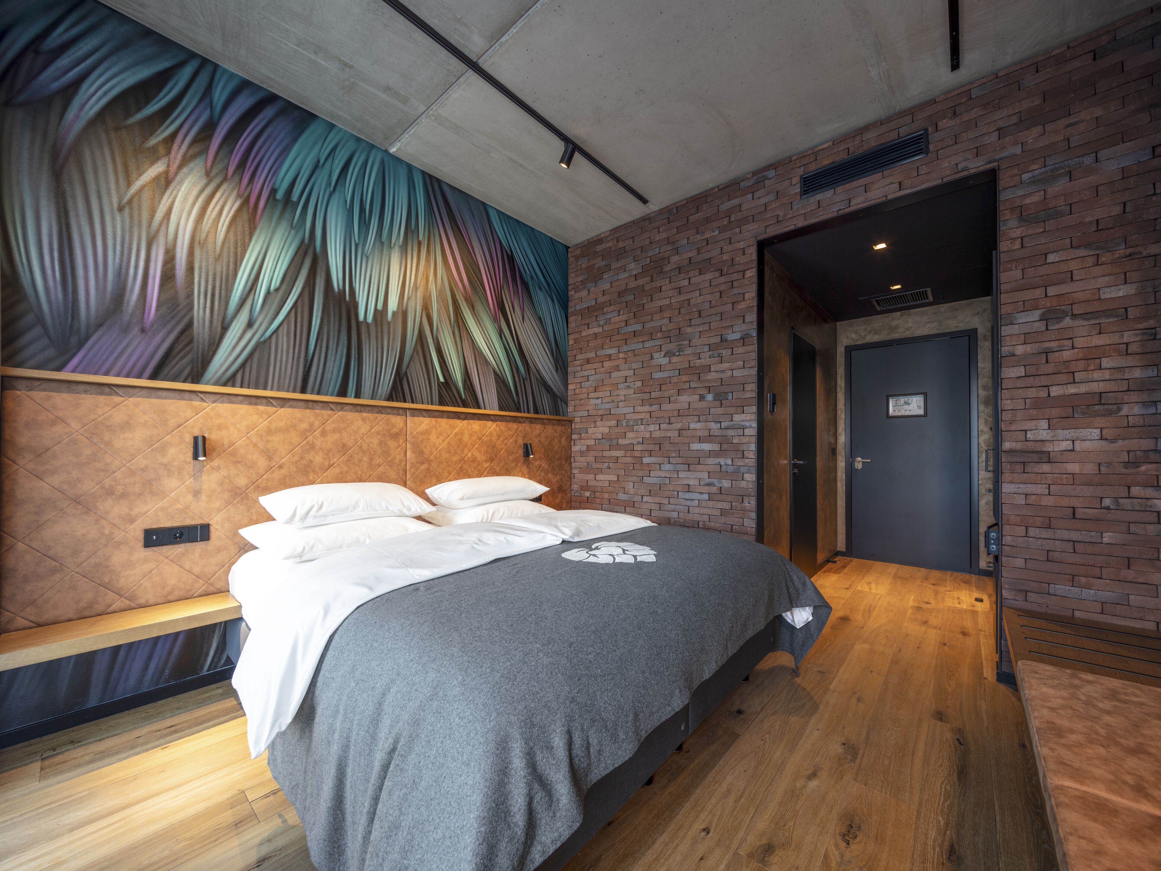 A modern hotel room with a large bed, a brick wall, and a mural on the ceiling.
