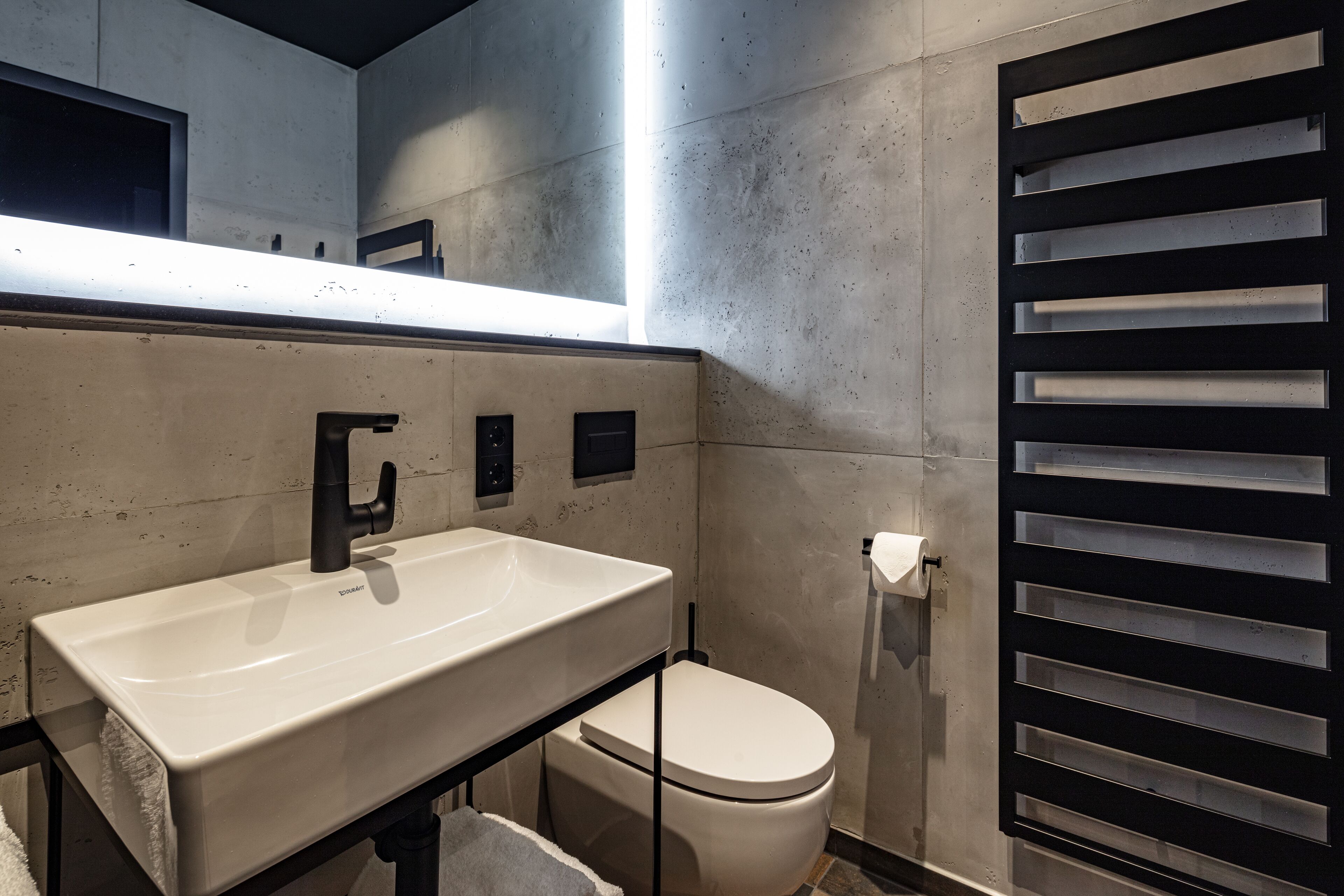 Un baño moderno con un lavamanos blanco, grifo negro y un inodoro.