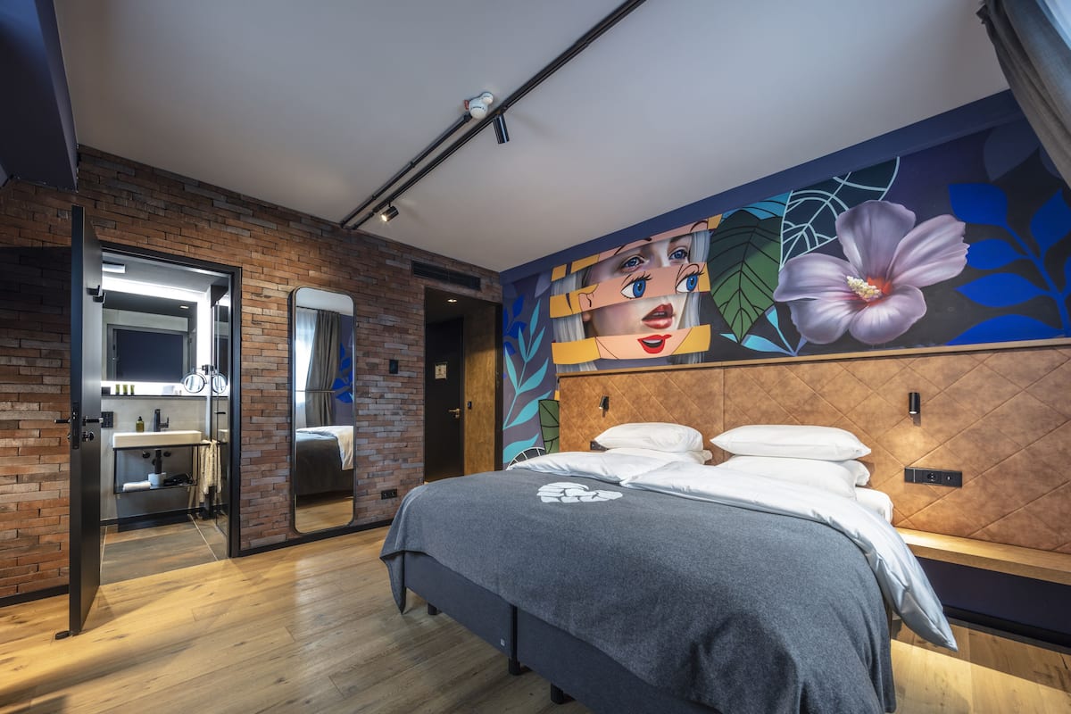 A modern bedroom with a large bed, a bathroom with a mirror, and a wall mural.