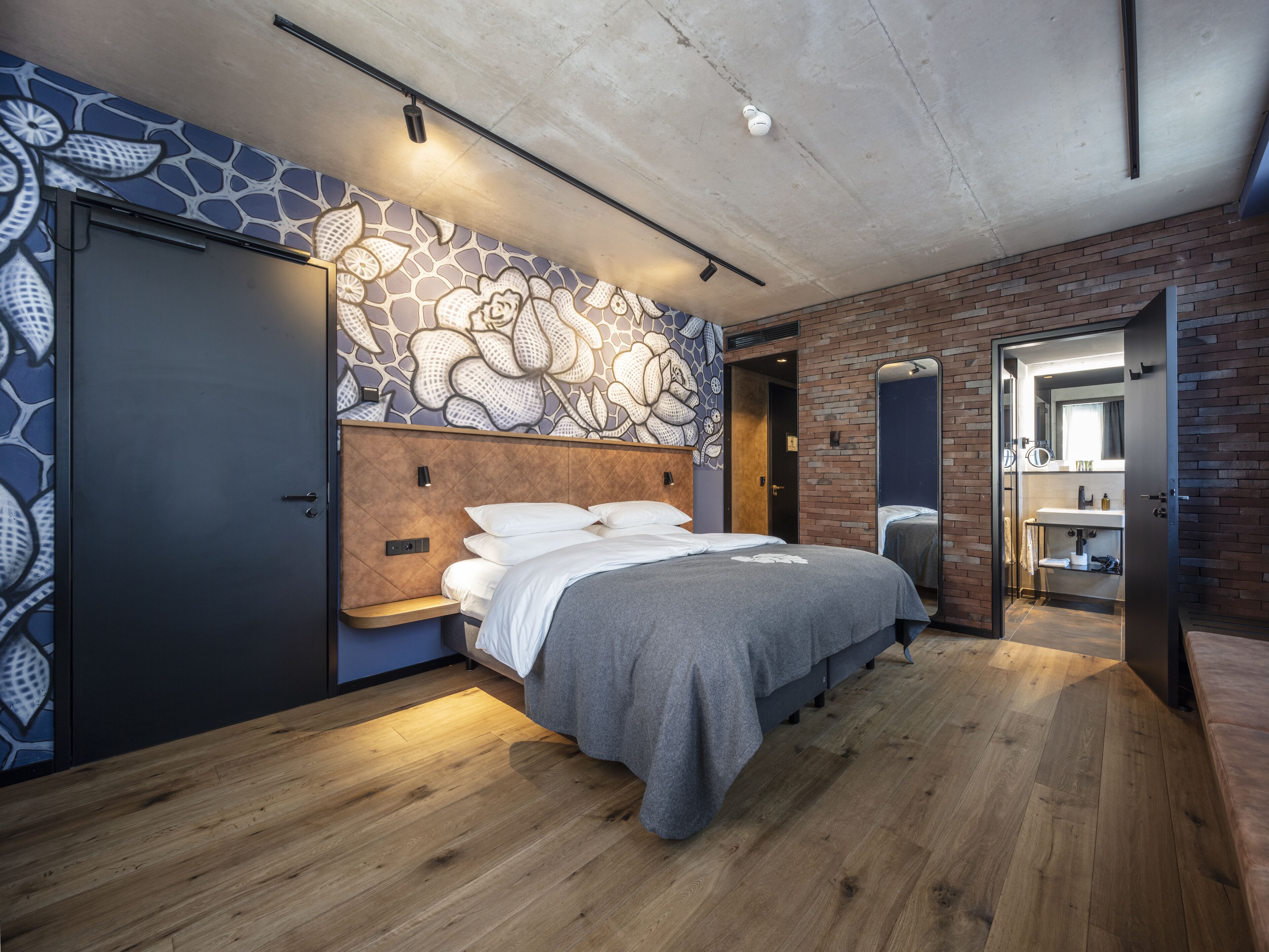 Une chambre moderne avec une tête de lit en bois, un grand lit, un banc intégré et un mur en briques.