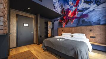 Una habitación de hotel moderna con una cama grande, piso de madera, pared de ladrillo y un cuadro abstracto de gran tamaño en la pared.