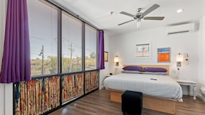 Un dormitorio moderno con un ventanal grande, un ventilador de techo y una cama con cabecera de madera.