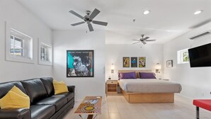 Ein modernes Schlafzimmer mit einem Bett, einem schwarzen Ledersofa, einem Holztisch und einem Deckenventilator.