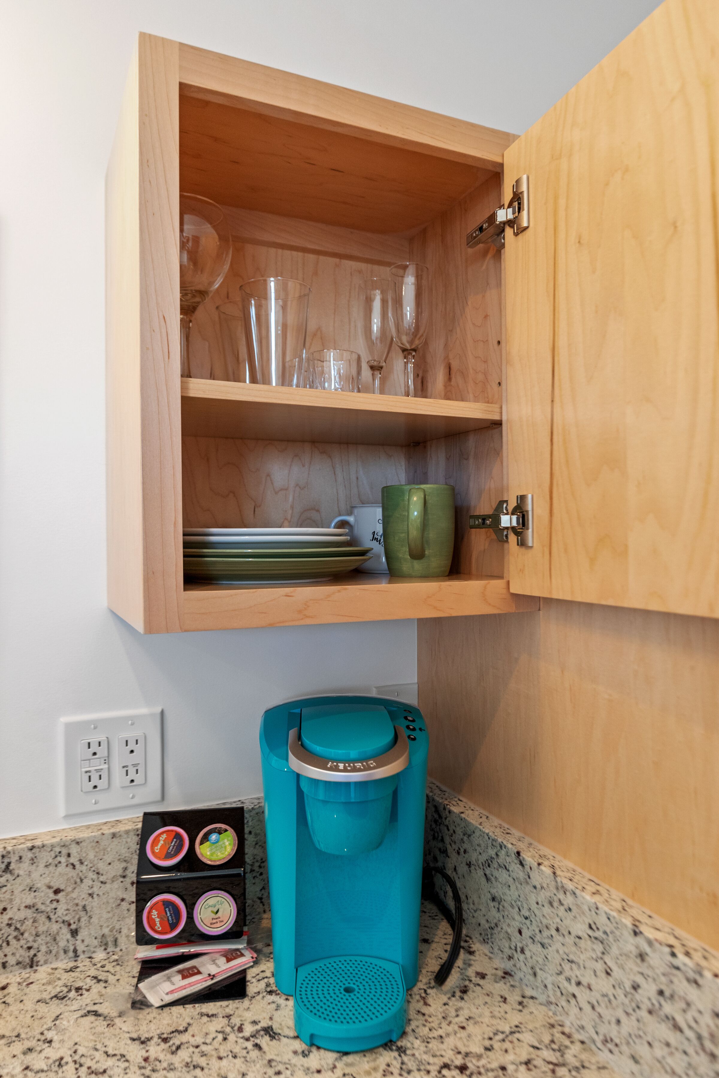 A kitchen with a wooden cabinet containing glassware and a coffee maker.