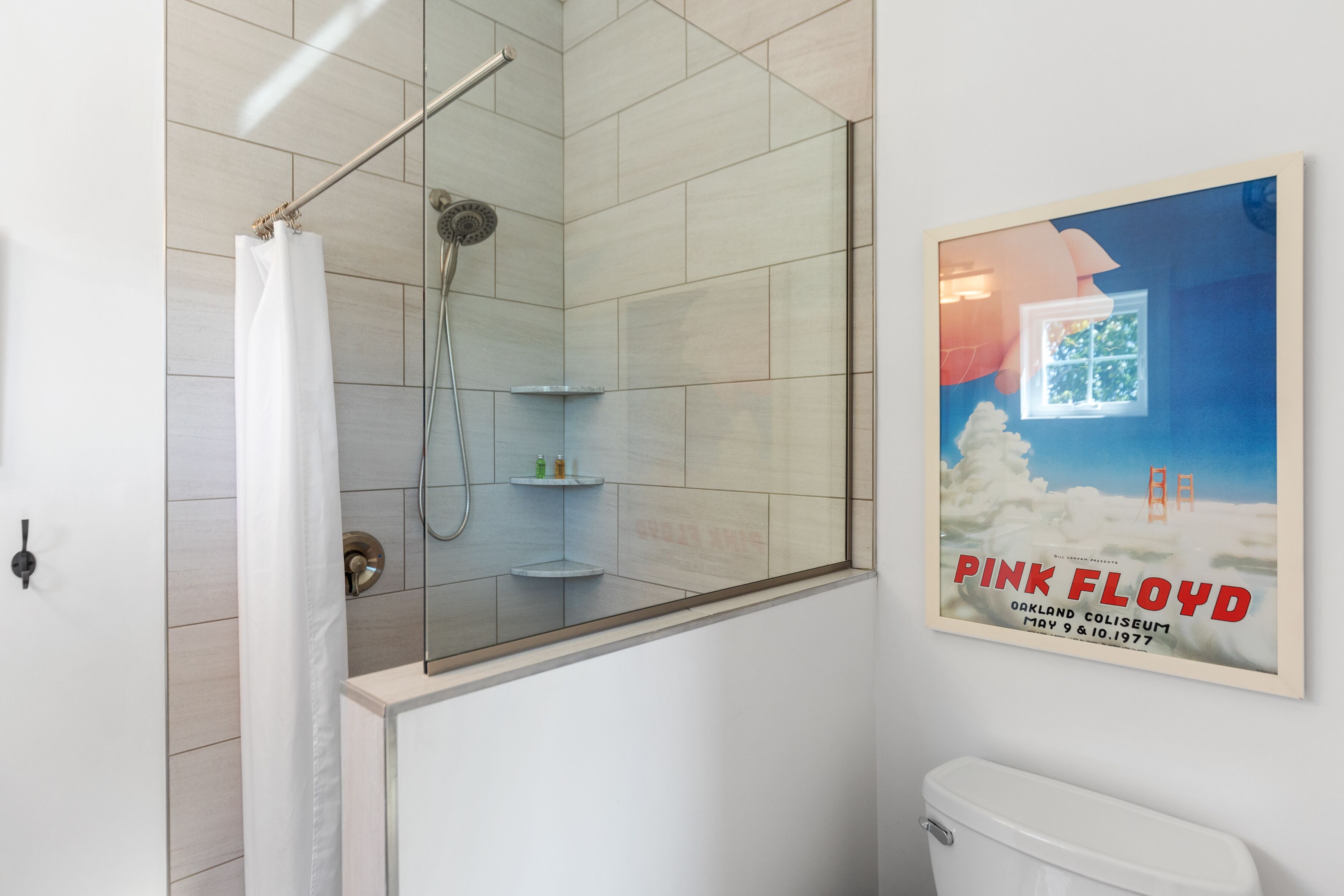 A bathroom with a glass shower enclosure, a toilet, and a poster on the wall.