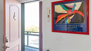A door with a number plate, a framed abstract painting, and a window with a view of greenery.