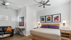 Een slaapkamer met een bed, nachtkastje, wandlamp en plafondventilator.