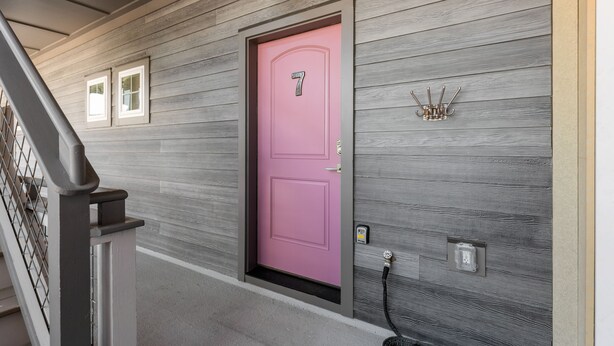 Une porte rose avec le numéro 7, un crochet en métal et une prise électrique, le tout sur un mur en bois.