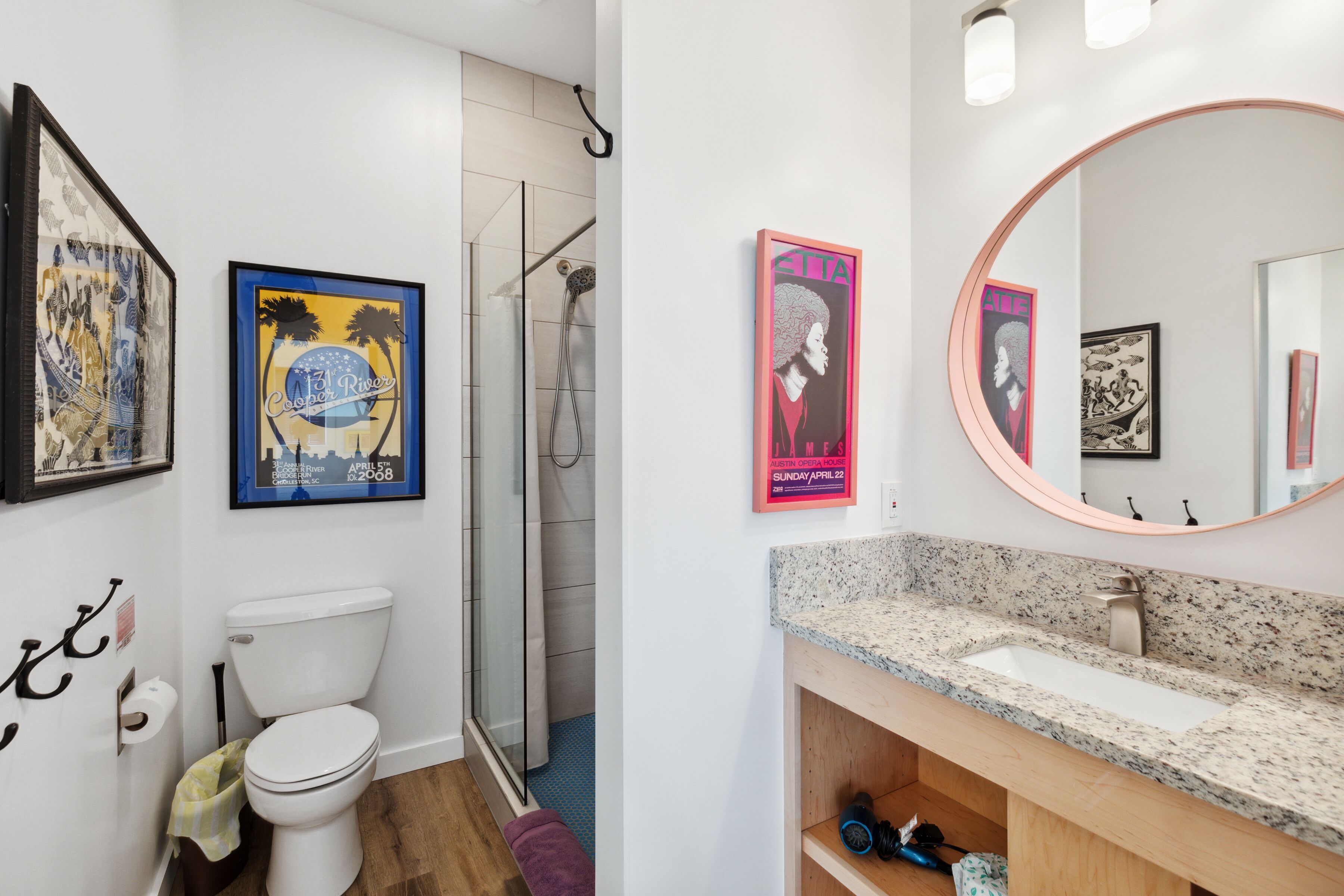 Ein Badezimmer mit Toilette, Dusche und Waschbecken. An den Wänden hängen Bilder in Rahmen und über dem Waschbecken befindet sich ein Spiegel.