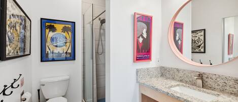 Ein Badezimmer mit Toilette, Dusche und Waschbecken. An den Wänden hängen Bilder in Rahmen und über dem Waschbecken befindet sich ein Spiegel.