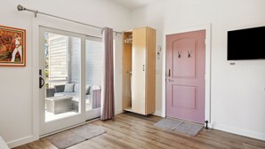 Una habitación con puerta de cristal corredera que da a un balcón, una puerta rosa y un armario de madera.