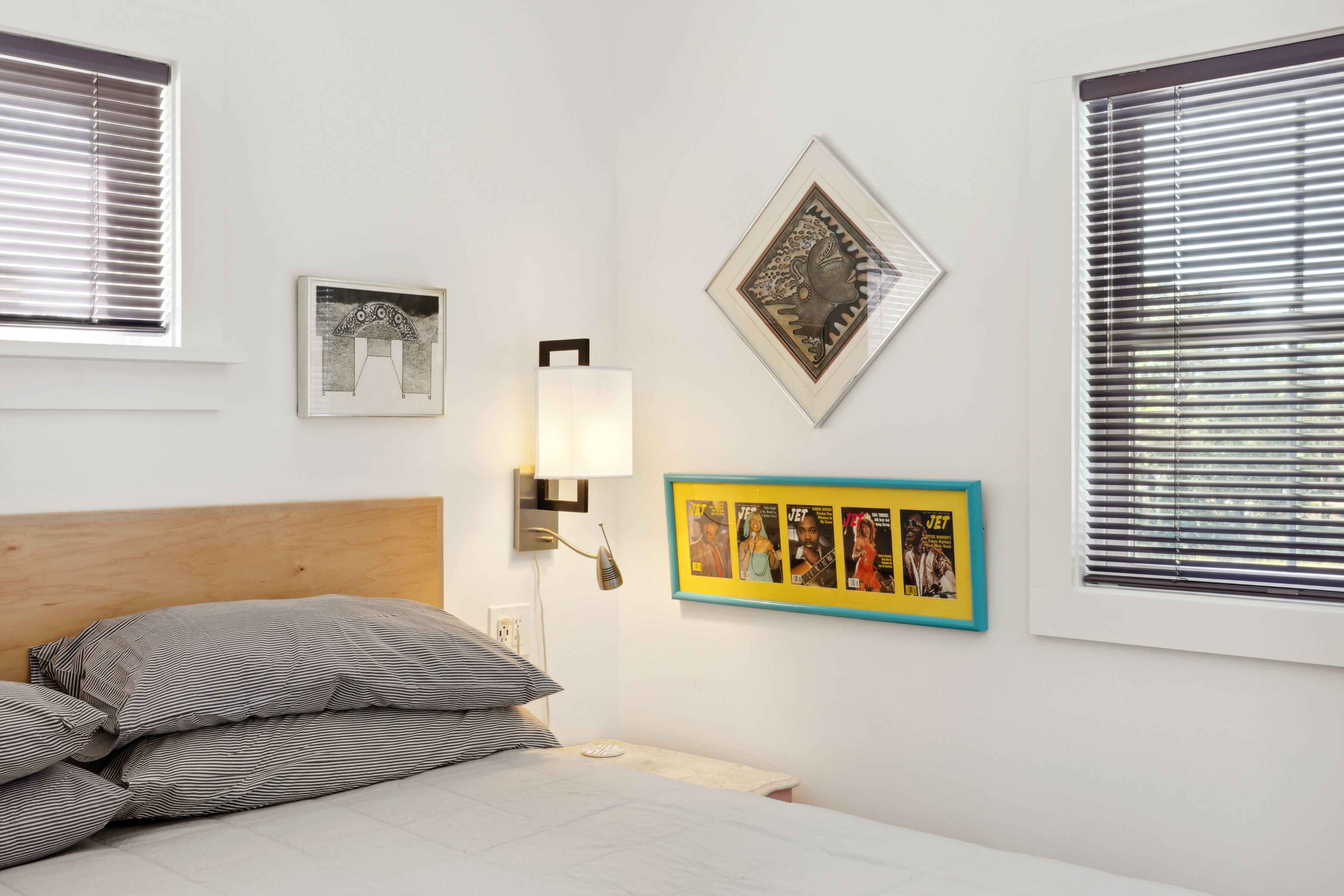 Un dormitorio con cama, almohadas, una lámpara de pared y cuadros enmarcados.