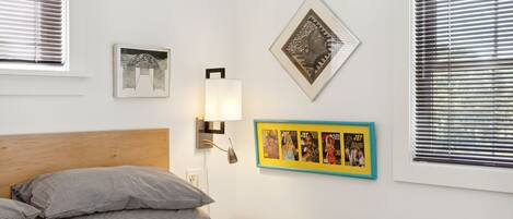Un dormitorio con cama, almohadas, una lámpara de pared y cuadros enmarcados.