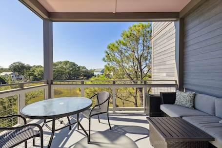 A covered outdoor area with a round table and chairs, a sofa, and a view of trees and houses.