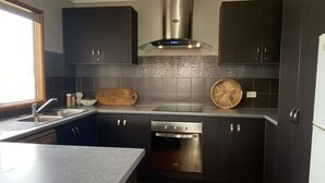 A modern kitchen with dark cabinets, stainless steel appliances, and a wooden cutting board on the counter. - Silver Seas - Plenty of space for family fun! Backyard Cricket Delight!! (Robe)