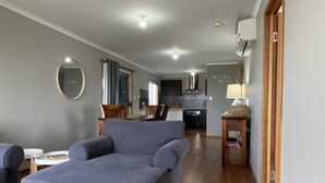 A modern living room with a grey sofa, a dining area with wooden chairs, and a kitchen in the background. - Silver Seas - Plenty of space for family fun! Backyard Cricket Delight!! (Robe)