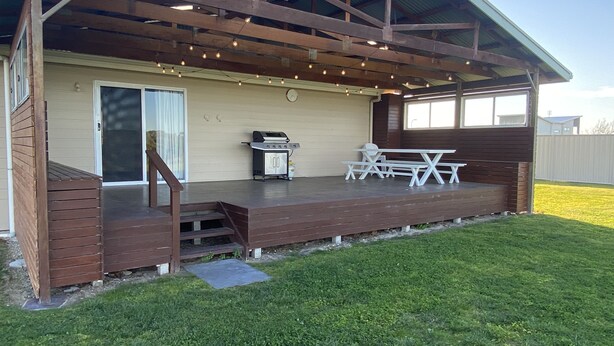 A covered patio with a grill, picnic table, and steps leading to a sliding door. - Silver Seas - Plenty of space for family fun! Backyard Cricket Delight!! (Robe)