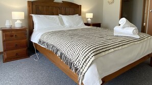 A neatly made bed with a patterned blanket, two bedside lamps, a wooden nightstand with drawers, and a towel on the bed. - Silver Seas - Plenty of space for family fun! Backyard Cricket Delight!! (Robe)