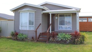 A single-story house with a front porch, a staircase leading to the entrance, and a small garden with various plants. - Silver Seas - Plenty of space for family fun! Backyard Cricket Delight!! (Robe)