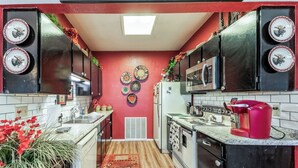 A kitchen with red walls, a microwave, a stove, and a sink. There are decorative plates on the wall and a red kettle on the counter. - Gotch Eyed Moose by Ruidoso Vacation Rentals (Alto)