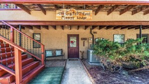 A rustic lodge entrance with a wooden staircase, a welcome bench, and a sign reading "The Gotch-Eyed Moose Lodge". - Gotch Eyed Moose by Ruidoso Vacation Rentals (Alto)