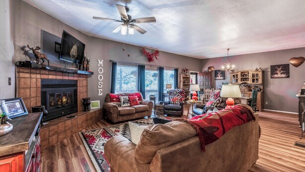 A cozy living room with a fireplace, a ceiling fan, and a TV mounted on the wall. - Gotch Eyed Moose by Ruidoso Vacation Rentals (Alto)