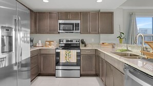 A modern kitchen with stainless steel appliances, wooden cabinets, and a large window providing natural light.
