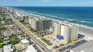 A coastal hotel with multiple floors, a parking lot, and a view of the ocean.