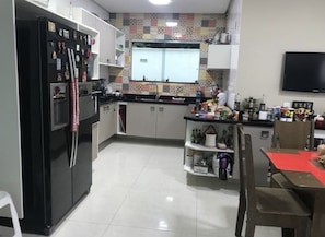 Uma cozinha moderna com geladeira preta, armários brancos, painel de azulejos e uma TV de tela plana na parede.