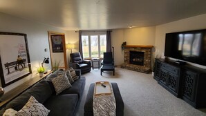 Un salon comprenant un canapé, des fauteuils, une cheminée, un téléviseur et un tableau encadré accroché au mur.
