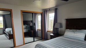 Une chambre à coucher avec un grand lit, une table de chevet, un miroir et une fenêtre avec des rideaux.