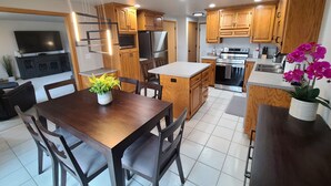 Une cuisine moderne avec des meubles en bois, des appareils en acier inoxydable et un coin repas comprenant une table et des chaises en bois.