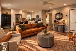 A modern living room with a leather sofa, a coffee table, and a dining area with a kitchen in the background. - The Tipsy Moon-New Hot Tub-Beautiful Mid-Century Modern Home-20min to Sedona (Cottonwood)